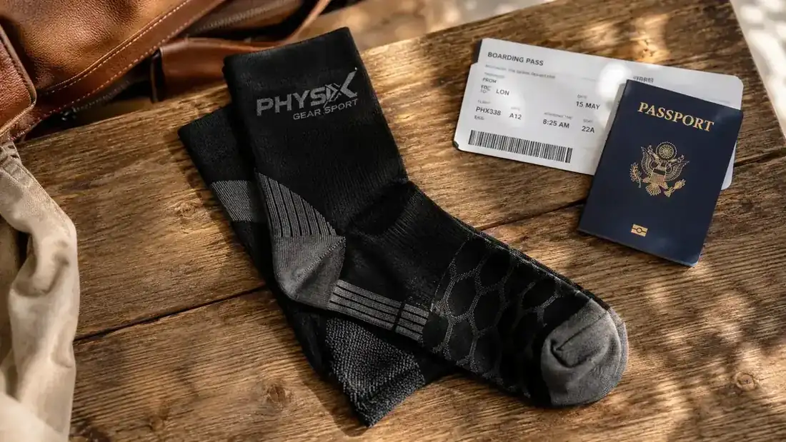 Pair of Physix Gear compression socks laid flat next to a boarding pass and passport on a wooden surface