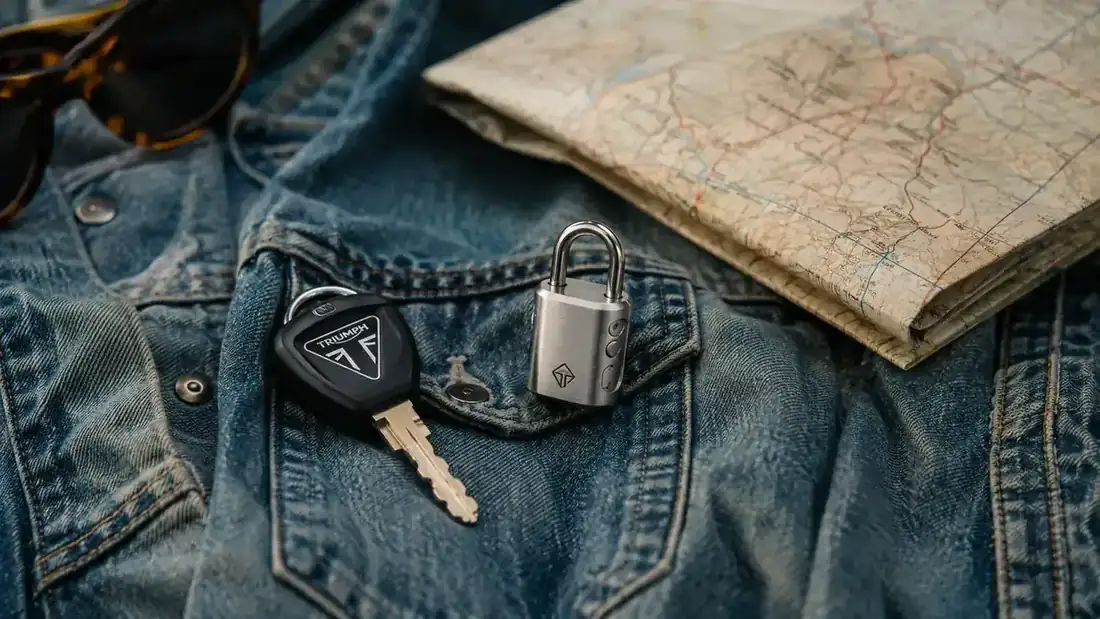 Compact Addalock device next to a motorcycle key and a folded paper map on a denim jacket