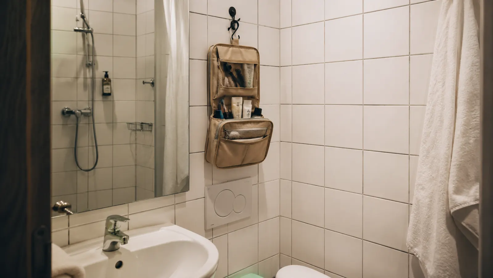 Travel toiletry bag packed and hanging in a hotel bathroom with no counter space available