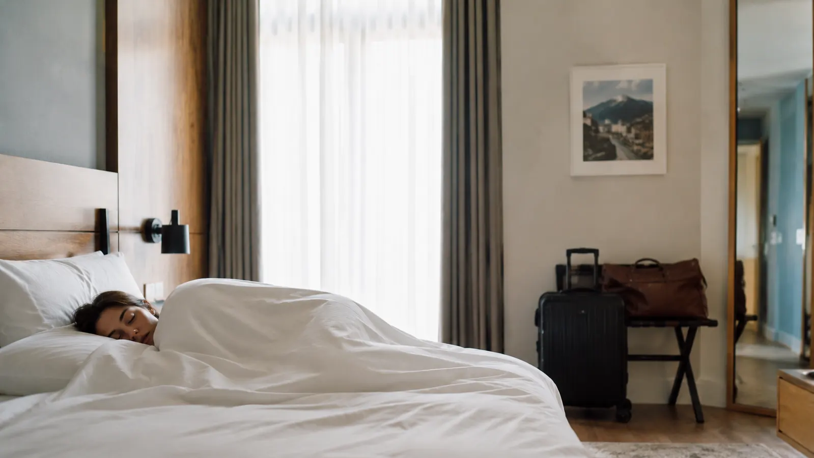 Traveler sleeping soundly in a hotel room with luggage tucked against the wall