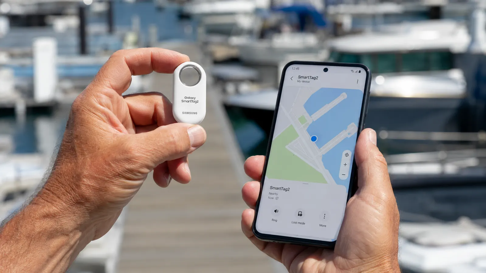 Hand holding a Samsung SmartTag2 next to a Galaxy phone showing the SmartThings Find app