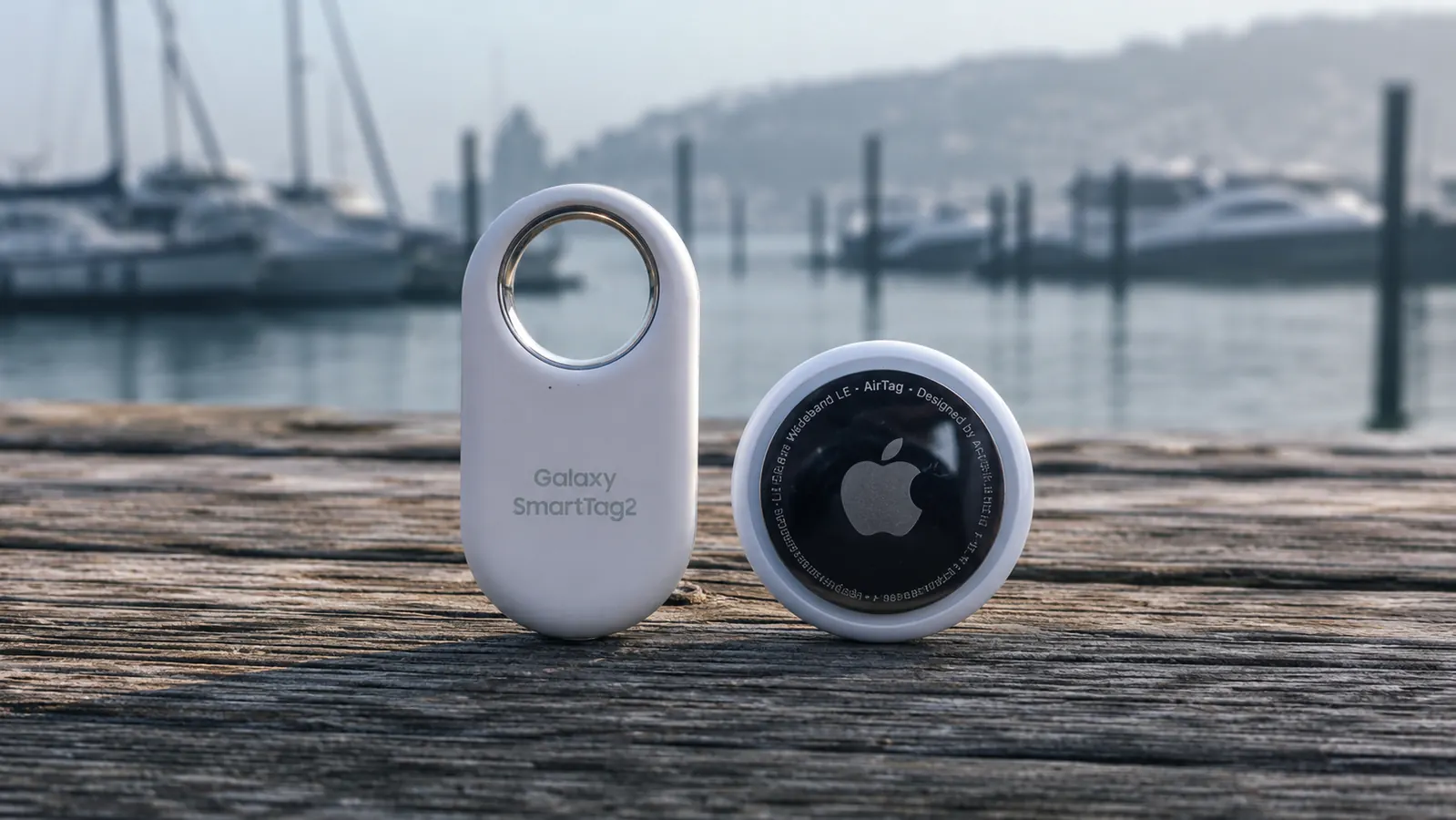 SmartTag2 next to Apple AirTag on a wooden dock surface showing size comparison