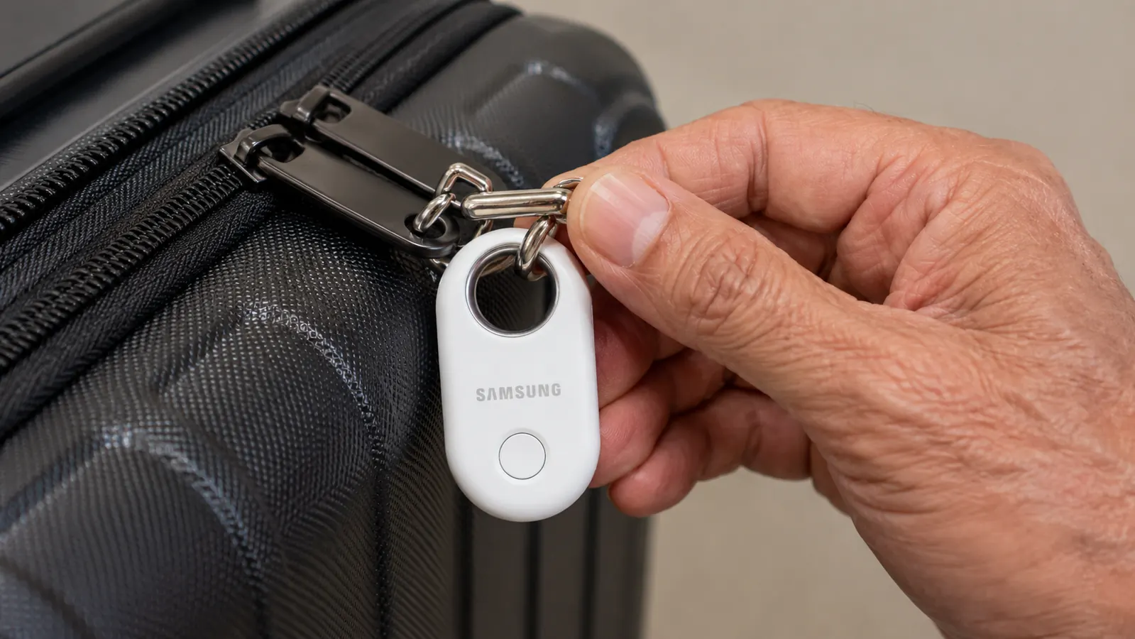 Close-up of Samsung SmartTag2 attached to a luggage zipper pull, showing the device size relative to a hand